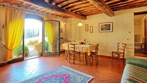Un coin repas avec une table dressée pour quatre personnes, des chaises en bois, un tapis et un plafond avec des poutres apparentes.