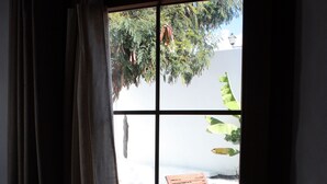 A window with a view of a wooden deck and a chair, curtains partially drawn, and a clear sky. - "TRIGO" quaint studio apartment in an old mill from the year 1912. (Maguez)