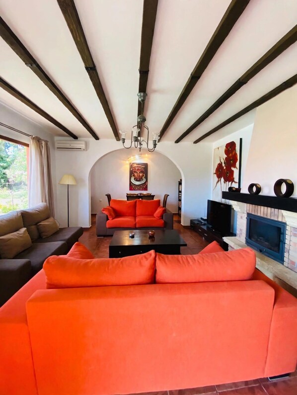 Una sala de estar con diseño moderno, que incluye un sofá grande color naranja, una mesa de centro negra y una chimenea.