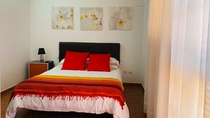 A bedroom with a bed, red pillows, a nightstand with a lamp, and three wall-mounted flower paintings. - Villa Nido Cari—Fuerteventura Rural Oasis (Casillas de Morales)