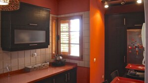 A compact kitchen with a microwave, a window with blinds, and a small dining area with a table and chairs. - Villa Nido Cari—Fuerteventura Rural Oasis (Casillas de Morales)