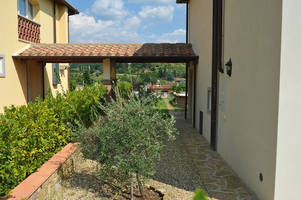 A covered outdoor area with a stone pathway, greenery, and a view of a village in the distance. - Private villa with pool in Greve in Chianti- Casa Amaranta (Greve in Chianti)