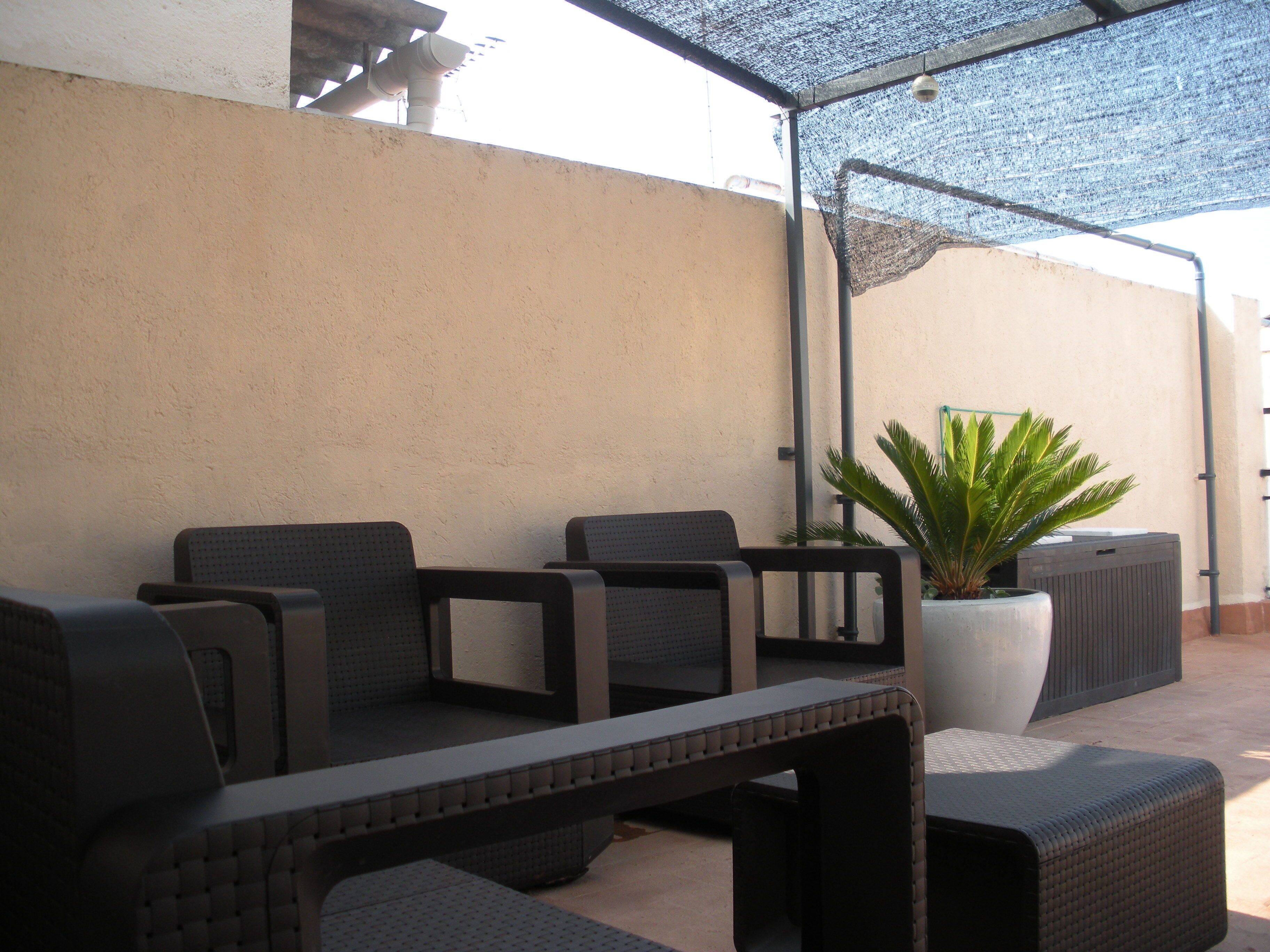 Un espace extérieur aménagé avec une table et des chaises, un pot de fleurs et une partie abritée.