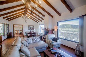 A spacious living room with a high ceiling, wooden beams, a large window with a view, a fireplace, and a dining area in the background. - Light & Spacious House in the Vineyard region, just in the middle of the island (Masdache ( Tías))