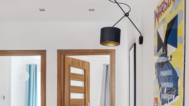 Een hal met houten vloer, een houten deur, een tafeltje met lamp en een poster aan de muur.