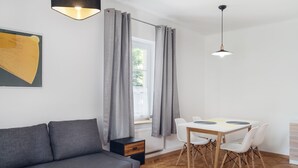 Een moderne kamer met een grijze bank, een vloer van houten visgraatmotief, een witte eettafel met stoelen en een raam met grijze gordijnen.
