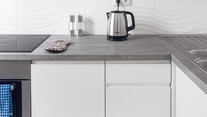 Een moderne keuken met witte en gele kastjes, een roestvrijstalen waterkoker en een zwart aanrecht.
