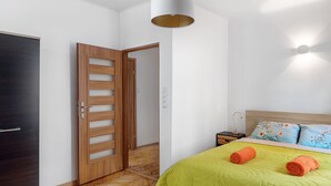 Een slaapkamer met een groen bedlaken, een houten deur en een nachtkastje met een lamp.