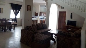 A spacious living area with a sofa set, a dining table, and chairs. There is a kitchen in the background with cabinets and a microwave. - Beachfront accommodation Yene - Senegal (Yene Kao)