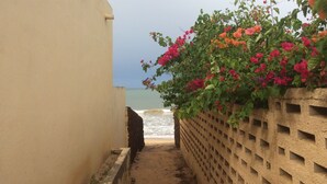 A narrow pathway leading to a beach with a wall on one side and a lattice fence on the other, overlooking the sea. - Beachfront accommodation Yene - Senegal (Yene Kao)