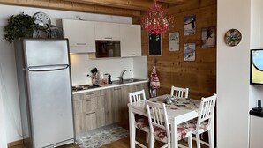 Eine kleine Küche mit Kühlschrank, Herd und Spüle, Holzboden und einem Essbereich mit Tisch und Stühlen.