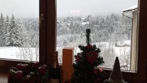 Ein Fenster mit Blick auf eine verschneite Landschaft, ein kleiner Weihnachtsbaum und eine Champagnerflasche auf der Fensterbank.