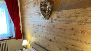 Ein Holzhütten-Zimmer mit einem Bett, roten Vorhängen, einem an der Wand befestigten Kranz und einer Nachttischlampe.