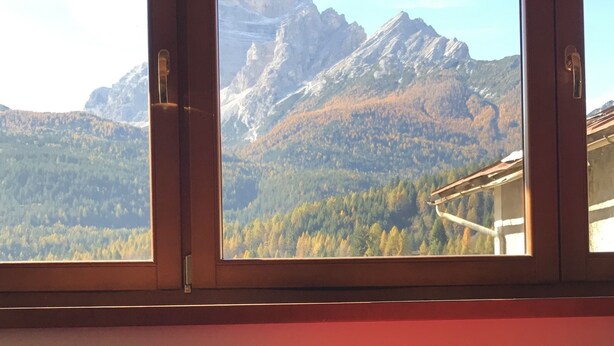 Ein Fenster mit Blick auf eine gebirgige Landschaft, einschließlich felsiger Gipfel und bewaldeter Flächen.