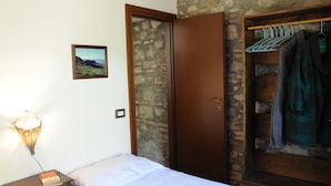 A bedroom with a wooden wardrobe, a hanging clothes rack, a bedside table with a lamp, and a framed picture on the wall. - Casa del Vento in San Cono, ancient stone dwelling among olive trees (Polizzi Generosa)