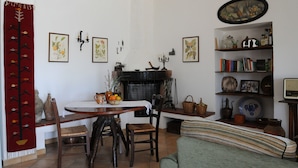 A dining area with a round table, chairs, a fireplace, and a bookshelf with books and decorative items. - Casa del Vento in San Cono, ancient stone dwelling among olive trees (Polizzi Generosa)