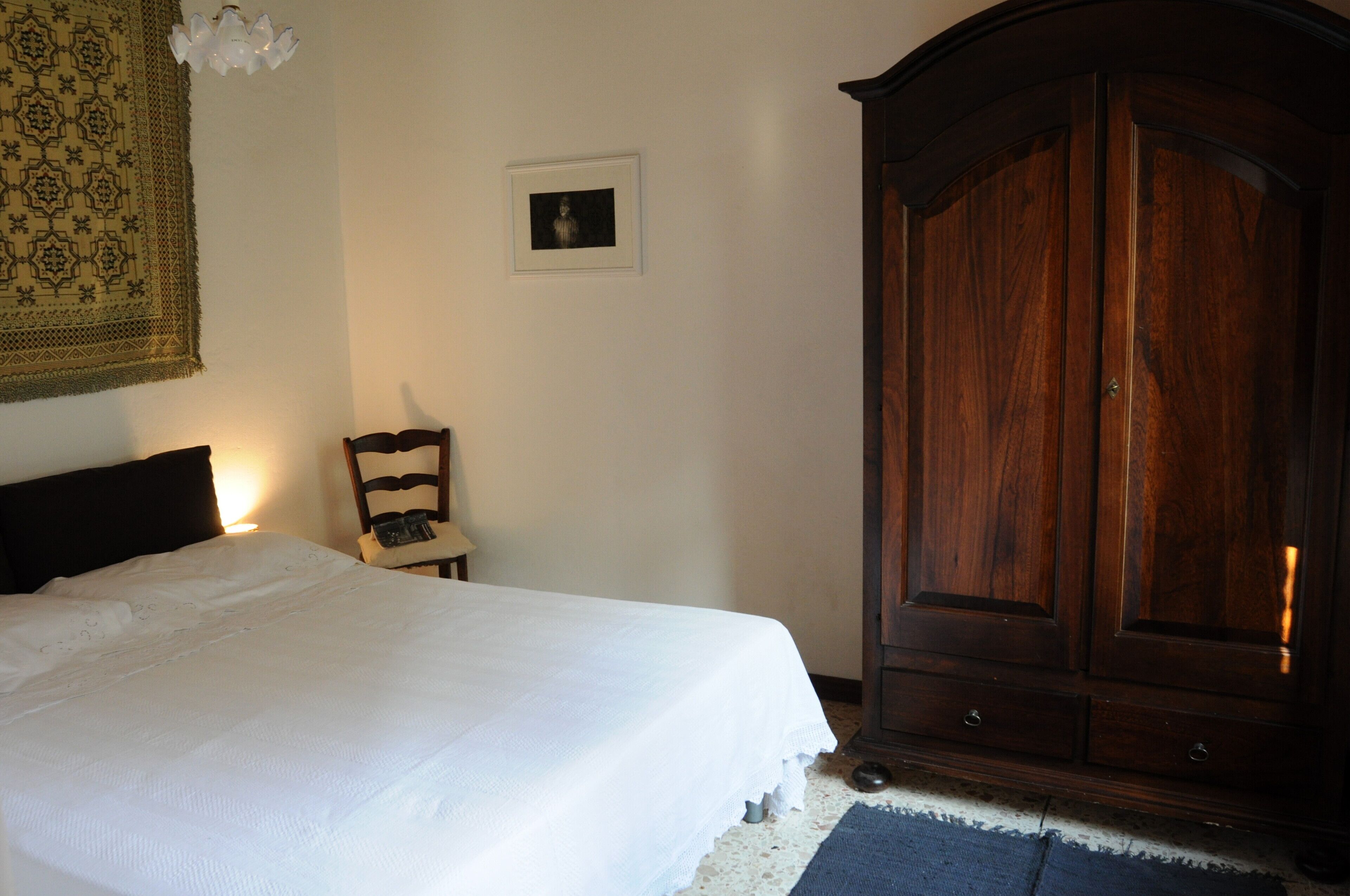 Une chambre à coucher comprenant un lit, une armoire en bois, une chaise, une petite table et un tableau accroché au mur.