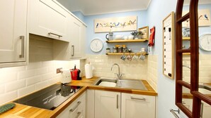 Une cuisine avec des meubles blancs, un plan de travail en bois, un évier et une horloge au mur.