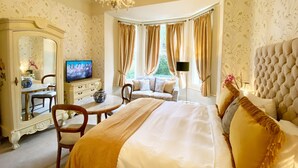 Une chambre à coucher luxueuse avec un grand lit, un coin salon avec un canapé et des fauteuils, une télévision, une commode et un miroir.
