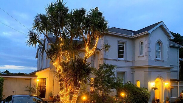 Une maison à deux étages avec une allée, une voiture garée et un arbre décoré de guirlandes lumineuses.