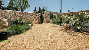 A gravel pathway leading to a stone wall with a doorway, surrounded by various plants and a street lamp. - The White House - Tavira Historic old town center (Tavira)