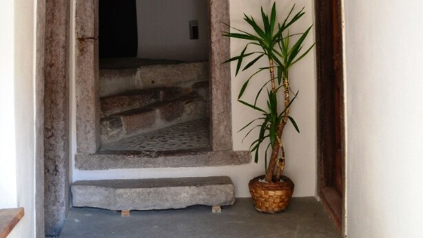 Ein schmaler Korridor mit Betonboden, einem Holztürrahmen und einem Blumentopf.