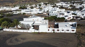 A coastal village with white buildings, some with flat roofs and others with sloped roofs. There are palm trees and a dirt road visible. - " MILLO" characteristic studio apartment in an old motor mill from the year 1912. (Maguez)
