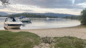 Un lago con barcos amarrados a la orilla, rodeado de zonas verdes y montañas al fondo.