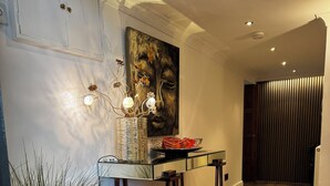 Un interior moderno con piso de madera, una consola de vidrio, una planta en maceta y un cuadro en la pared.