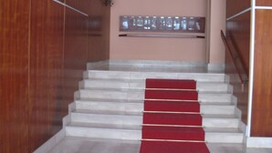 Un escalier recouvert d’une moquette rouge, des murs en bois et une fenêtre avec des stores.