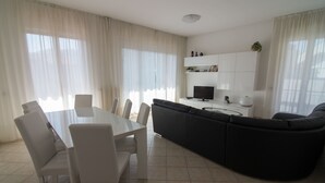 Un salon moderne comprenant une table à manger, des chaises, un canapé noir, un téléviseur et un meuble agrémenté d’objets décoratifs.