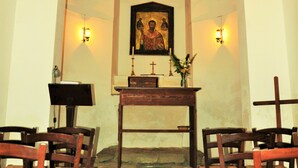 Interior de iglesia con bancales de madera, un altar de madera y un cuadro religioso enmarcado.