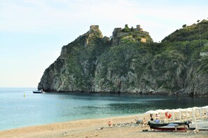A beach with boats, a rocky cliff, and a castle-like structure.