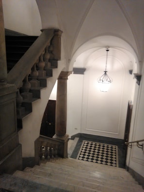 Uma escadaria com piso xadrez que leva a uma porta com luminária pendente.