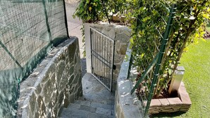 Eine steinerne Treppe führt zu einem verschlossenen Eingang, umgeben von Grünpflanzen und einer Steinmauer.