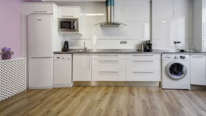 Une cuisine moderne avec des meubles blancs, un four à micro-ondes en acier inoxydable, une machine à café et un lave-linge.
