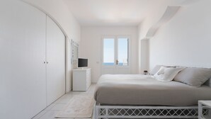 Un dormitorio con cama, armario, mesita de noche y vista al mar a través de una puerta.