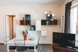 Un salon moderne comprenant une table à manger, des chaises, un téléviseur et des étagères intégrées où sont rangés des livres et des objets décoratifs.