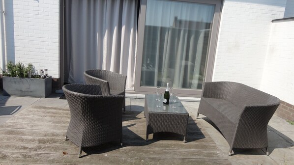 An outdoor patio with wicker furniture, a glass table, and a bottle of champagne.