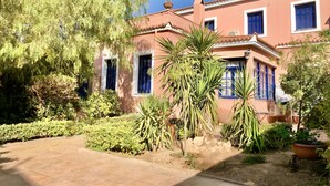 A building with a pink facade, blue shutters, and a tiled courtyard. - Traditional Villa Aegina Port (Aigina)