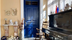 A room with a blue door, a piano, a chair, and a vase with dried plants. - Traditional Villa Aegina Port (Aigina)