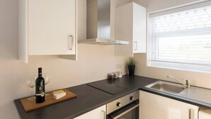 A modern kitchen with white cabinets, a stainless steel sink, and a window with blinds. - Amazing Duplex Apartment (Greater London)