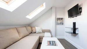 A modern living room with a sofa, a coffee table, a TV, and a skylight. - Amazing Duplex Apartment (Greater London)