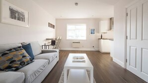 A modern living room with a sofa, coffee table, and a dining area with chairs. - Amazing Duplex Apartment (Greater London)