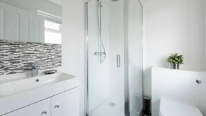 A modern bathroom with a glass shower enclosure, a white sink with a black and white tiled backsplash, and a toilet. - Amazing Duplex Apartment (Greater London)