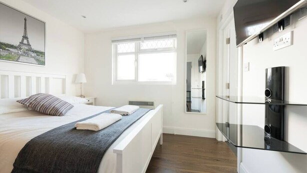 A modern hotel room with a bed, a window, a mirror, and a built-in TV shelf. - Amazing Duplex Apartment (Greater London)