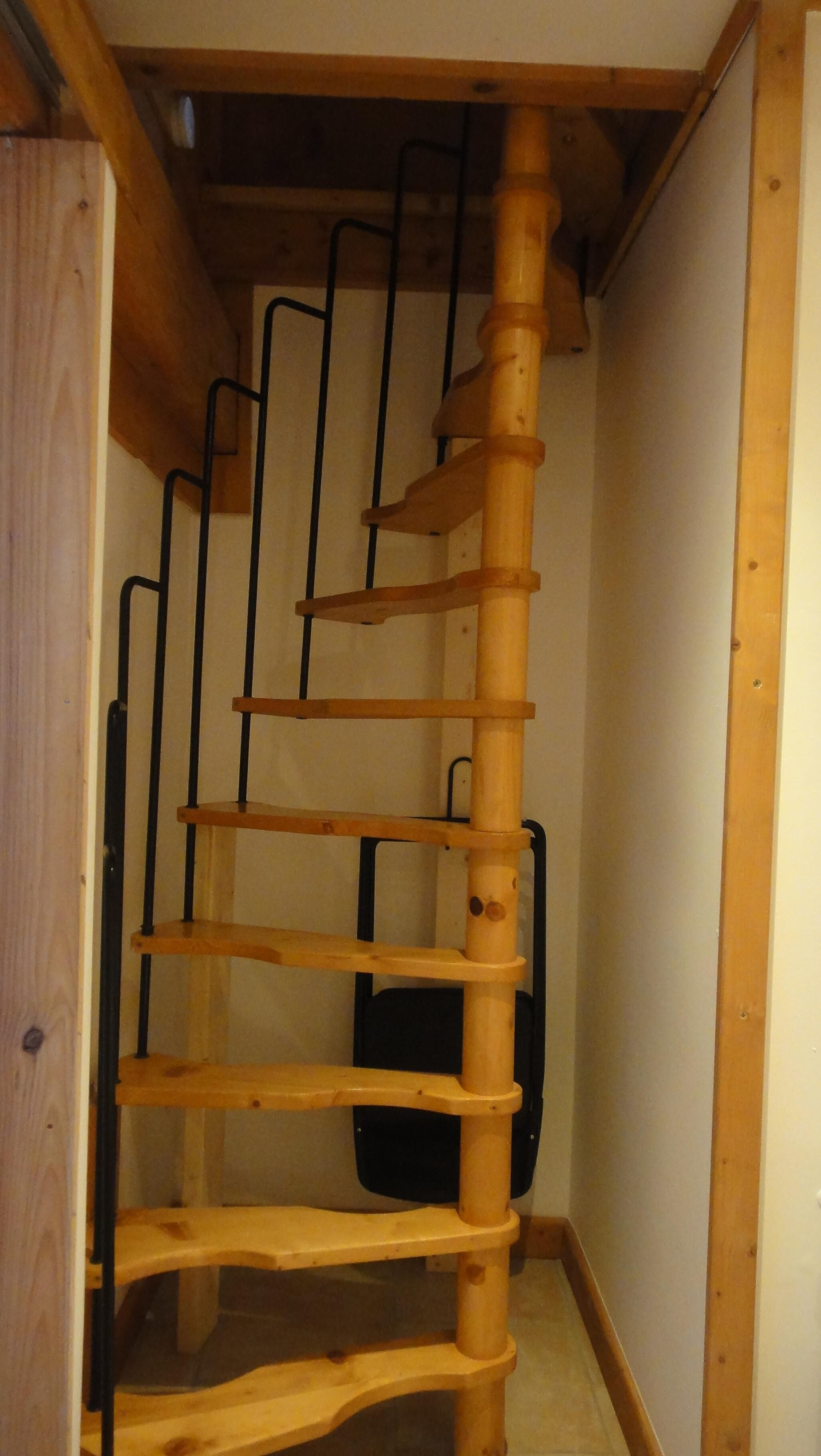 Una escalera en espiral de madera con barandillas de metal negro, que conduce a un piso superior.