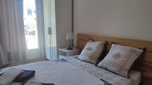 Una cama bien hecha con almohadas y toallas dobladas, una mesita de noche con una lámpara y vistas al exterior a través de una ventana.