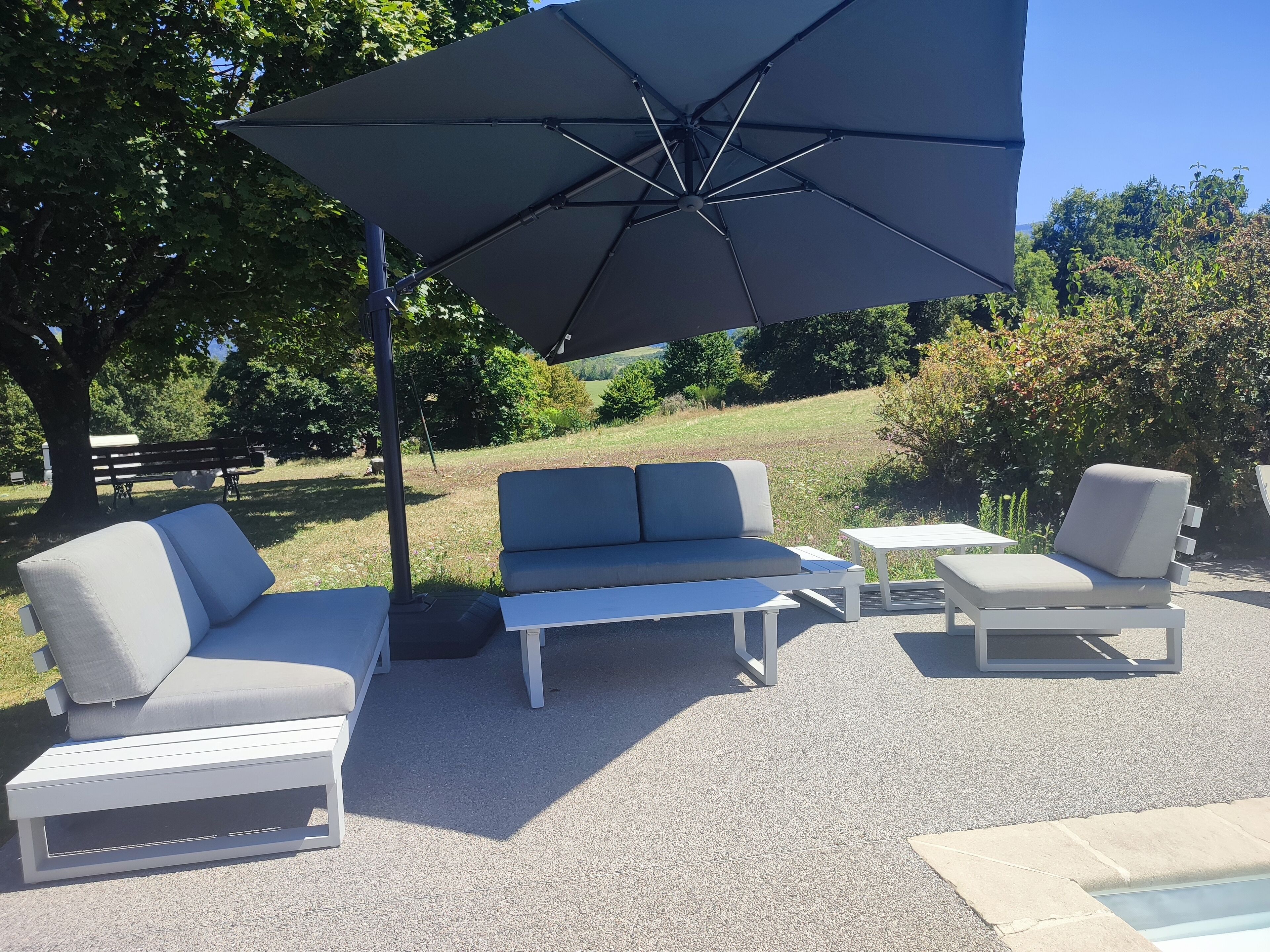 Een terras met een grote parasol, een bank, een tafel en een stoel.