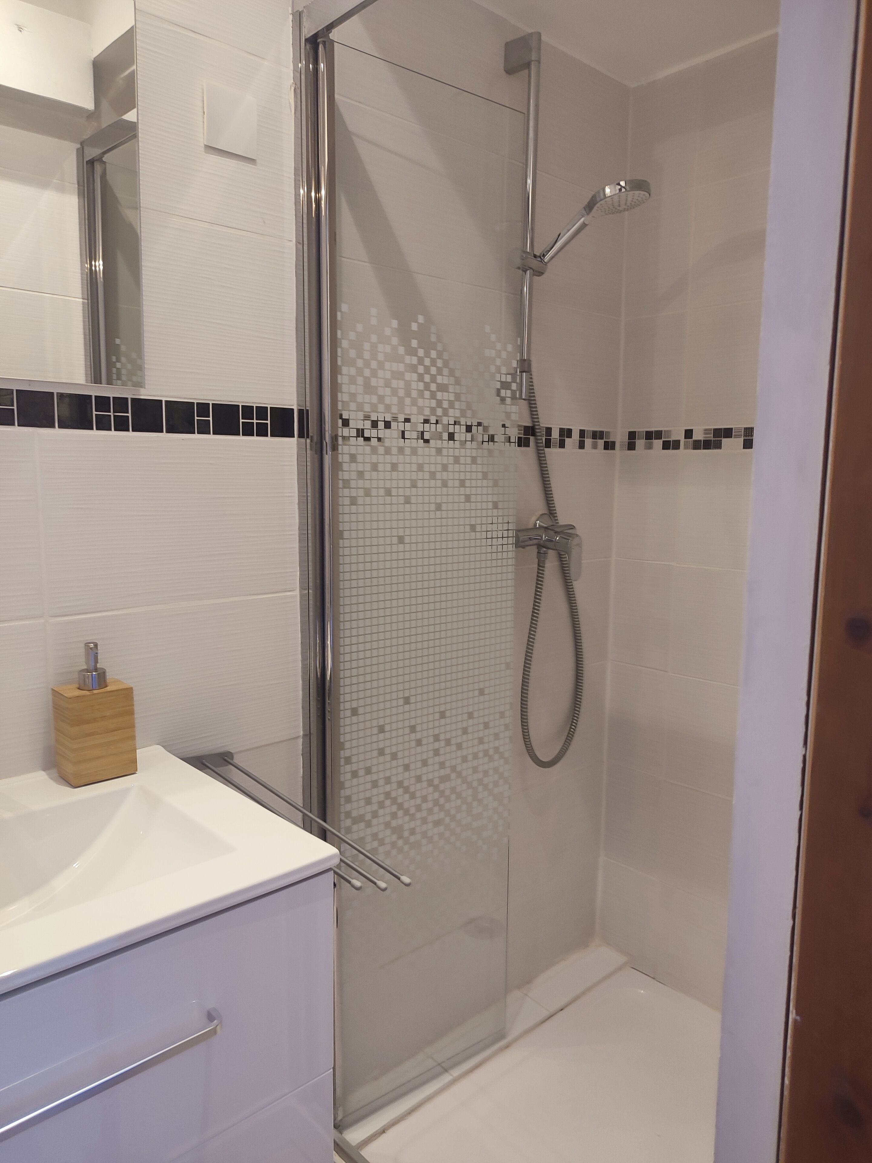 A modern bathroom with a glass-enclosed shower, white tiles, and a wooden soap dispenser.
